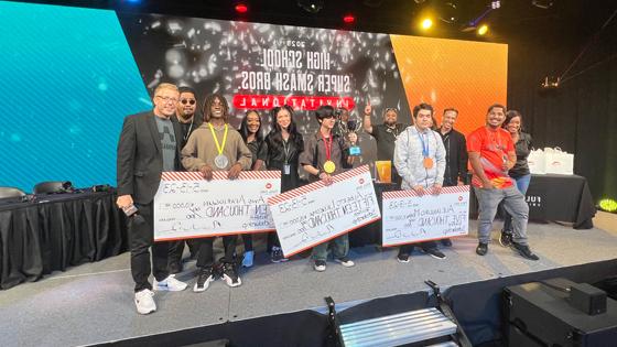 Techfest tournament winners holding large scholarship checks on stage alongside 满帆 staff members in the Fortress.